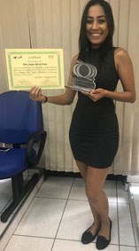 A foto apresenta a aluna Thais Campos Reis de Souza segurando o certificado do prêmio Mário Tolentino e sorrindo.