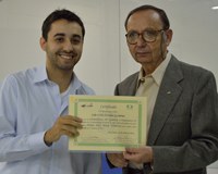 A foto apresenta o discente João Pedro Fermino Gutierrez sorrindo, junto ao professor Julio Zukerman Schpector, ambos segurando o certificado do prêmio Mário Tolentino.